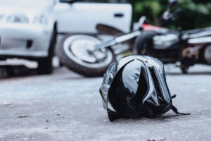 Close-up of a black biker helmet on the street with overturned motorbike in the background.